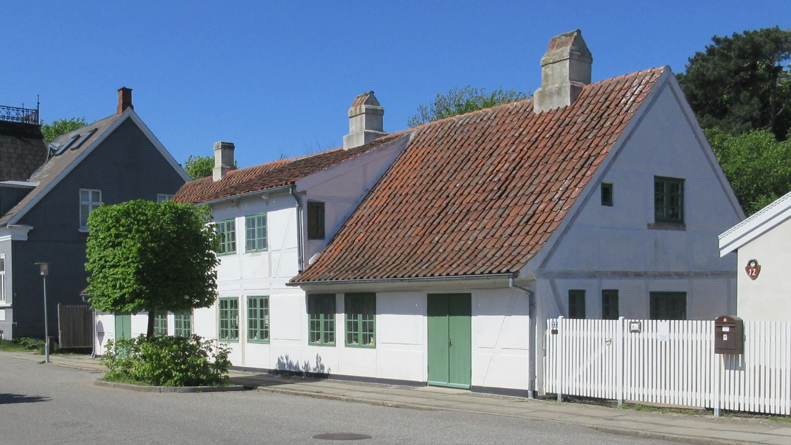 Strandgade i Frederiksværk med hvide huse, grønne døre og træer langs vejen.